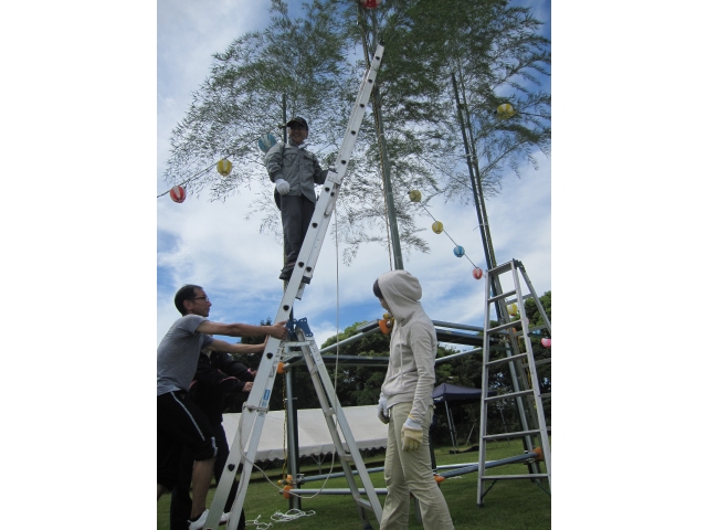 夏祭りの準備を行っています。寮長がはしごに上ってやぐらの設置作業を行っています。